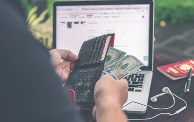 A person in front of a laptop pulling American money out of their wallet