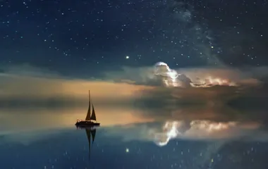 A small sailboat on calm water with the reflection of the nigh sky 