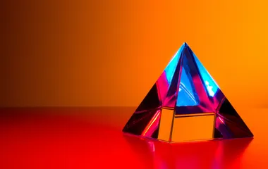 A glass pyramid on an orange table and background reflecting the blue sky