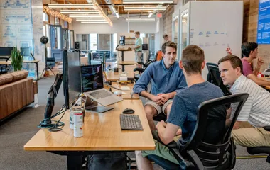 Three people talking in an open plan office about code.